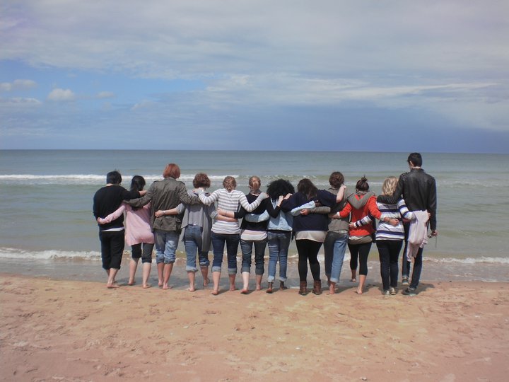 group of students on a beach facing away from the camera with their arms on each other's shoulders
